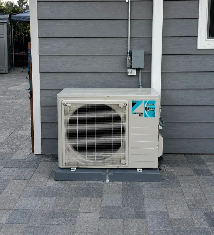 Daikin ductless outdoor AC unit mounted on a pad next to a home