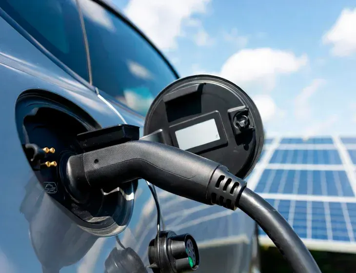 EV charging station connected to an electric vehicle with solar panels in the background. Comprehensive solar and EV services in Agoura Hills, CA.