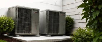 Two modern outdoor HVAC condenser units installed side by side on concrete pad next to house