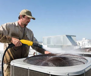 Professional HVAC technician pressure washing outdoor air conditioning unit coils on rooftop in Thousand Oaks